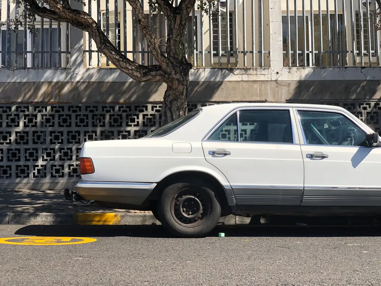Classic white car parked under a tree on a sunny Cape Town street, highlighting urban retro style.