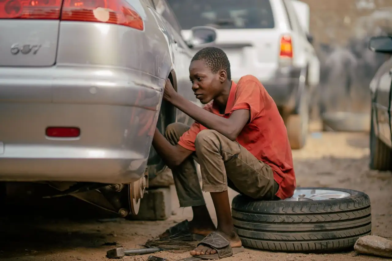 Young mechanic focused on repairing a car tire in an outdoor garage.