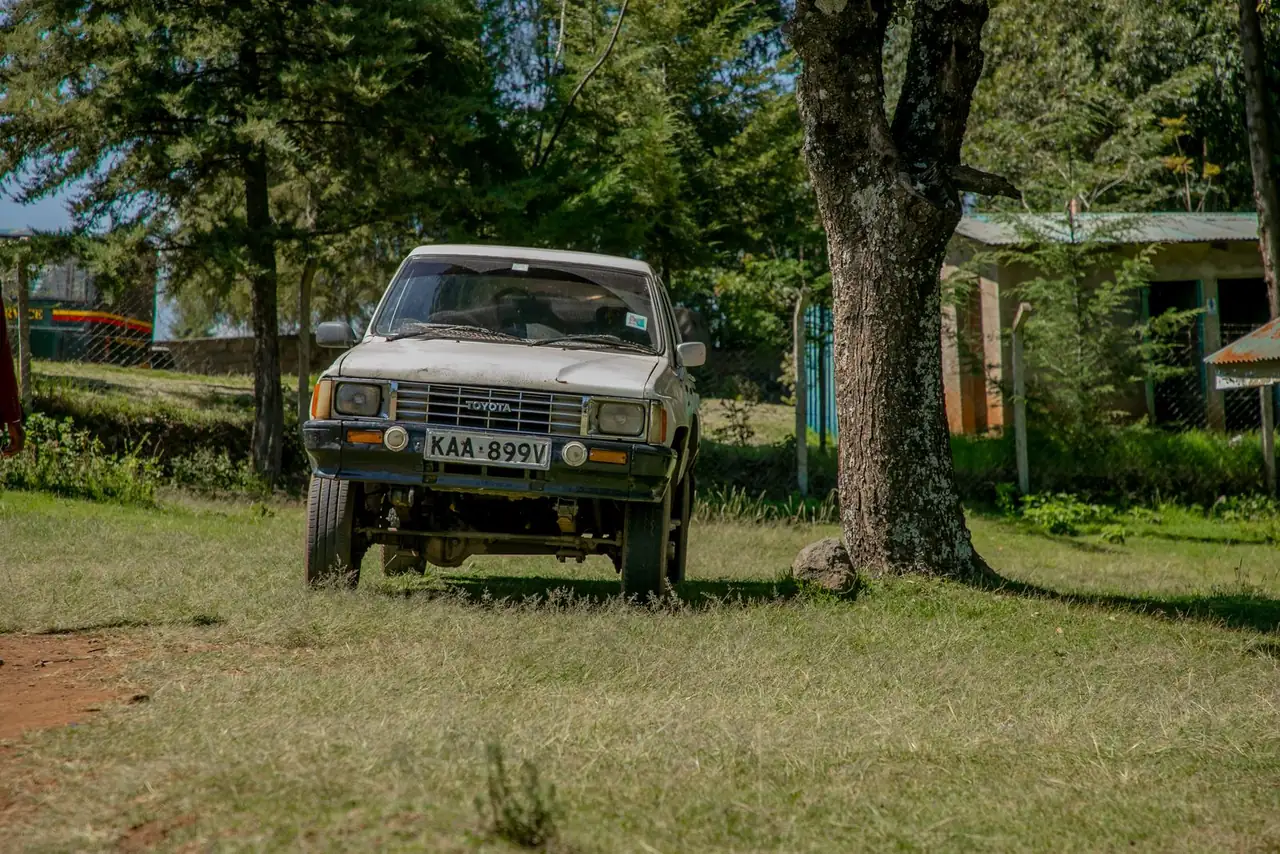 Toyota SUV parked on grassy rural area in Kenya with surrounding trees and buildings.